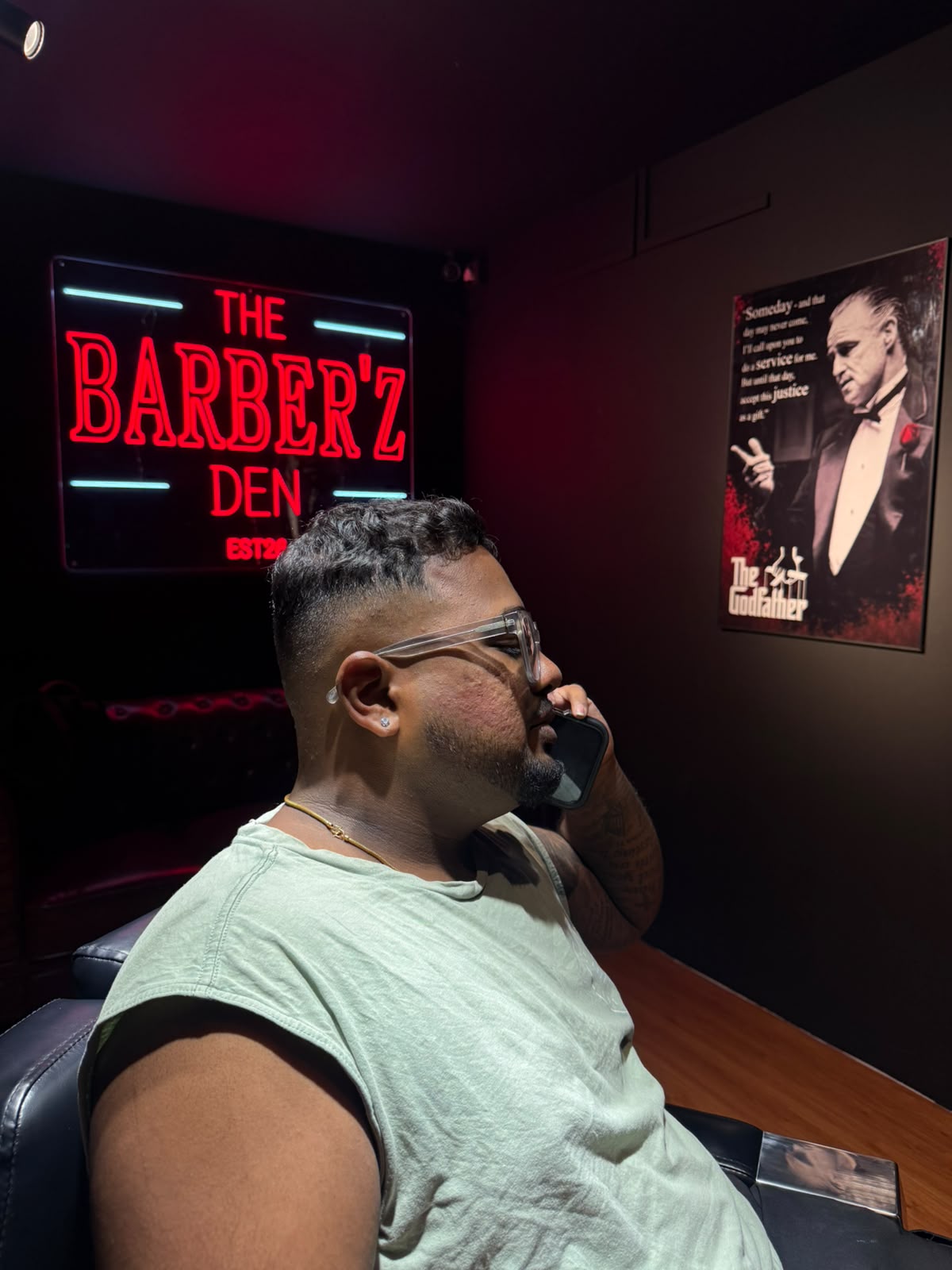 Customer with a fresh fade seated beneath The Barber'Z Den neon sign